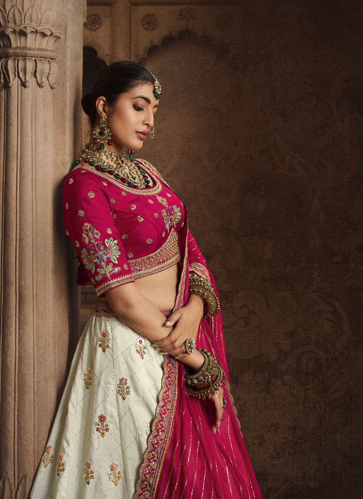 Image: Women in Magenta Pink & Off White Color Designer Wedding Wear Lehenga Choli with Embroidery Work. The lehenga choli features intricate embroidery in magenta pink and off white colors. The design showcases a beautiful blend of traditional and contemporary elements.