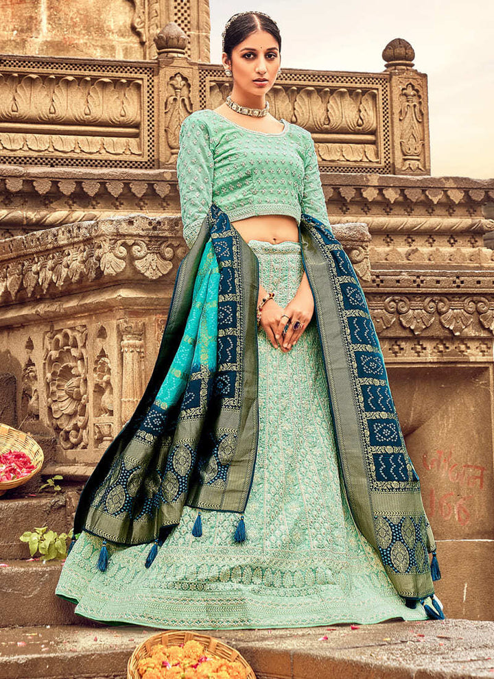 Woman in Sea green Elegant Designer Lehenga Cholis with Lakhnavi Work. This exquisite ensemble showcases a delightful cream color and is adorned with intricate Lakhnavi work. The designer lehenga choli exudes elegance and charm, making it a perfect choice for weddings and special occasions. With its stunning craftsmanship and graceful appeal, this outfit is sure to make the wearer stand out with sophistication and style.