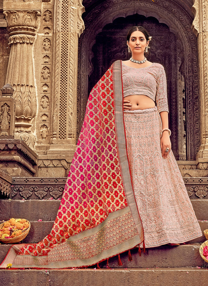 Woman in Light Pink Elegant Designer Lehenga Cholis with Lakhnavi Work. This exquisite ensemble showcases a delightful cream color and is adorned with intricate Lakhnavi work. The designer lehenga choli exudes elegance and charm, making it a perfect choice for weddings and special occasions. With its stunning craftsmanship and graceful appeal, this outfit is sure to make the wearer stand out with sophistication and style.