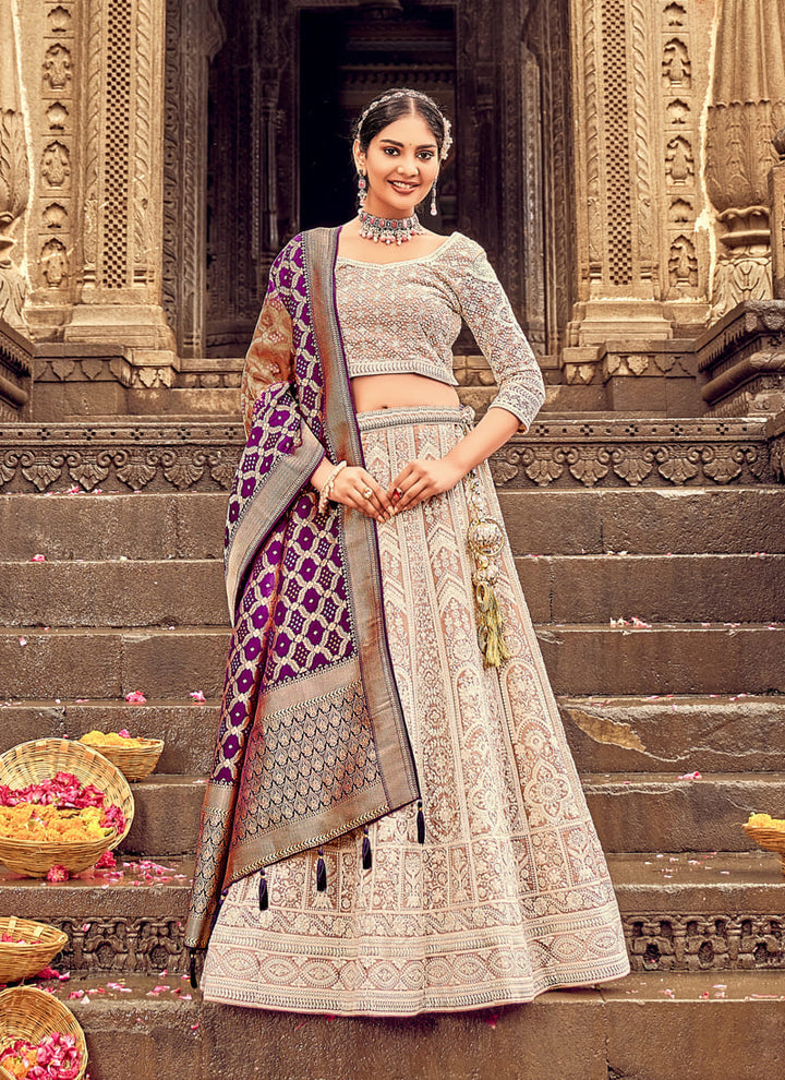 Woman in Beige Elegant Designer Lehenga Cholis with Lakhnavi Work. This exquisite ensemble showcases a delightful cream color and is adorned with intricate Lakhnavi work. The designer lehenga choli exudes elegance and charm, making it a perfect choice for weddings and special occasions. With its stunning craftsmanship and graceful appeal, this outfit is sure to make the wearer stand out with sophistication and style.