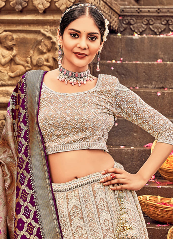 Woman in Beige Elegant Designer Lehenga Cholis with Lakhnavi Work. This exquisite ensemble showcases a delightful cream color and is adorned with intricate Lakhnavi work. The designer lehenga choli exudes elegance and charm, making it a perfect choice for weddings and special occasions. With its stunning craftsmanship and graceful appeal, this outfit is sure to make the wearer stand out with sophistication and style.