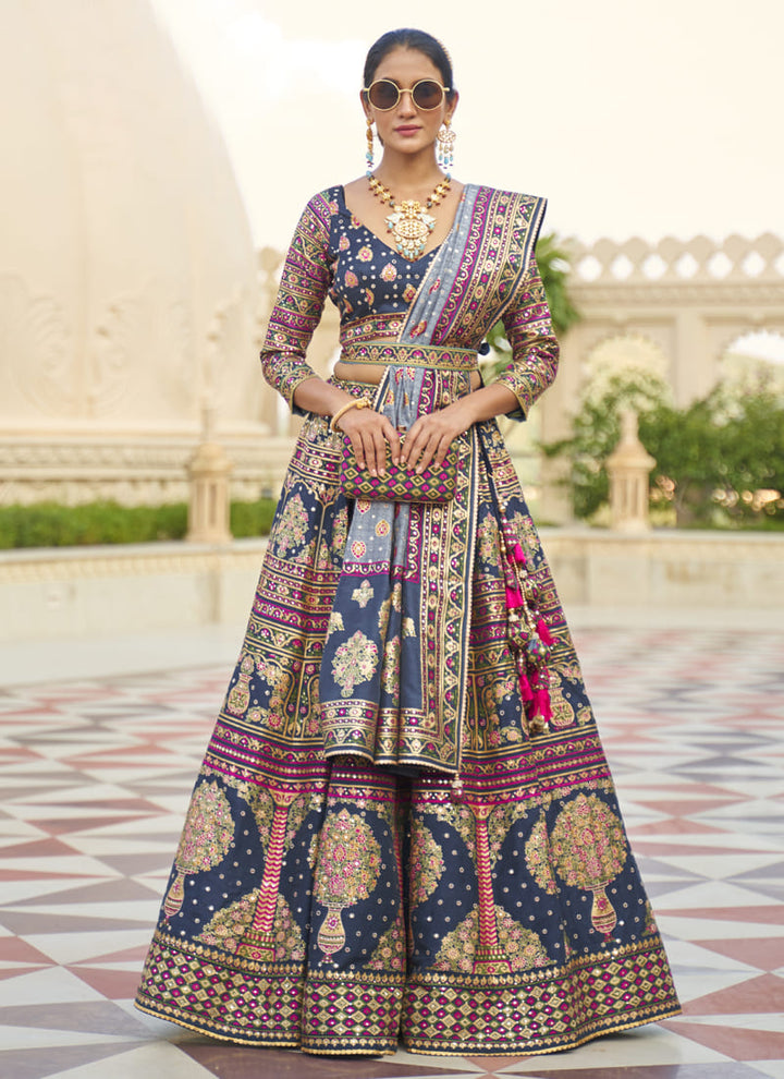 Image: Women in Navi Blue Radiant Smooth Rajwadi Silk Lehenga Choli. This mesmerizing ensemble showcases a radiant and smooth texture, made from luxurious Rajwadi silk. The lehenga choli exudes elegance and charm, perfect for special occasions and weddings. With its exquisite craftsmanship and glamorous appeal, this outfit is sure to make the wearer stand out with sophistication and style.